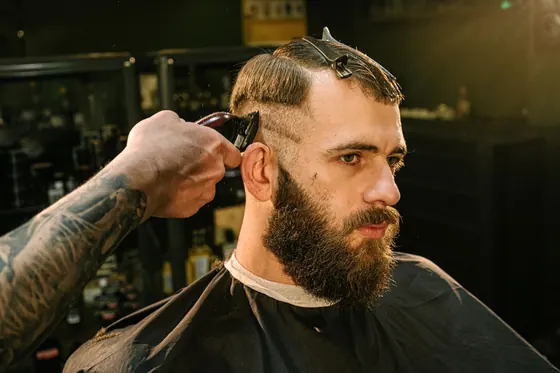 Barbero cortando el cabello a un cliente con barba en una barbería