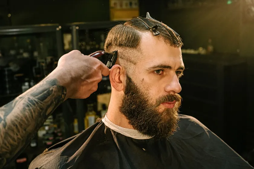 Barbero cortando el cabello a un cliente con barba en una barbería
