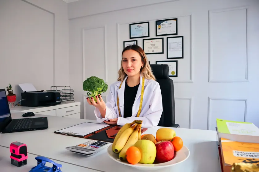 Nutrióloga en su consultorio con un brócoli en la mano y un frutero sobre el escritorio