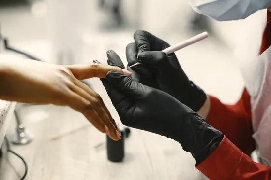 Manicurista con guantes aplicando esmalte en las uñas de una clienta