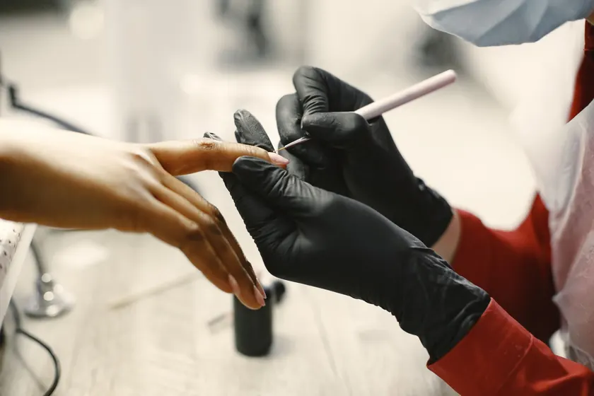 Manicurista con guantes aplicando esmalte en las uñas de una clienta